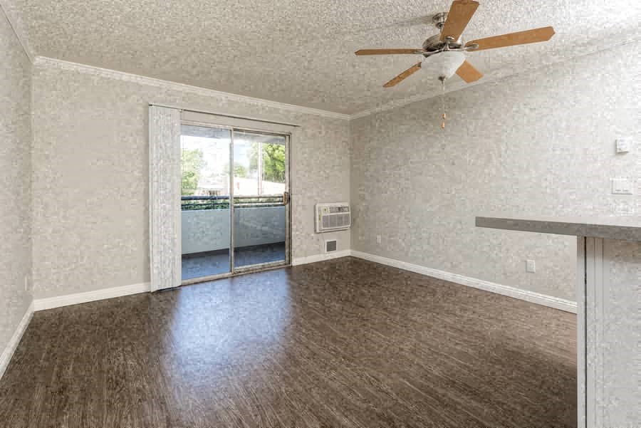 an empty living room with a ceiling fan and a balcony