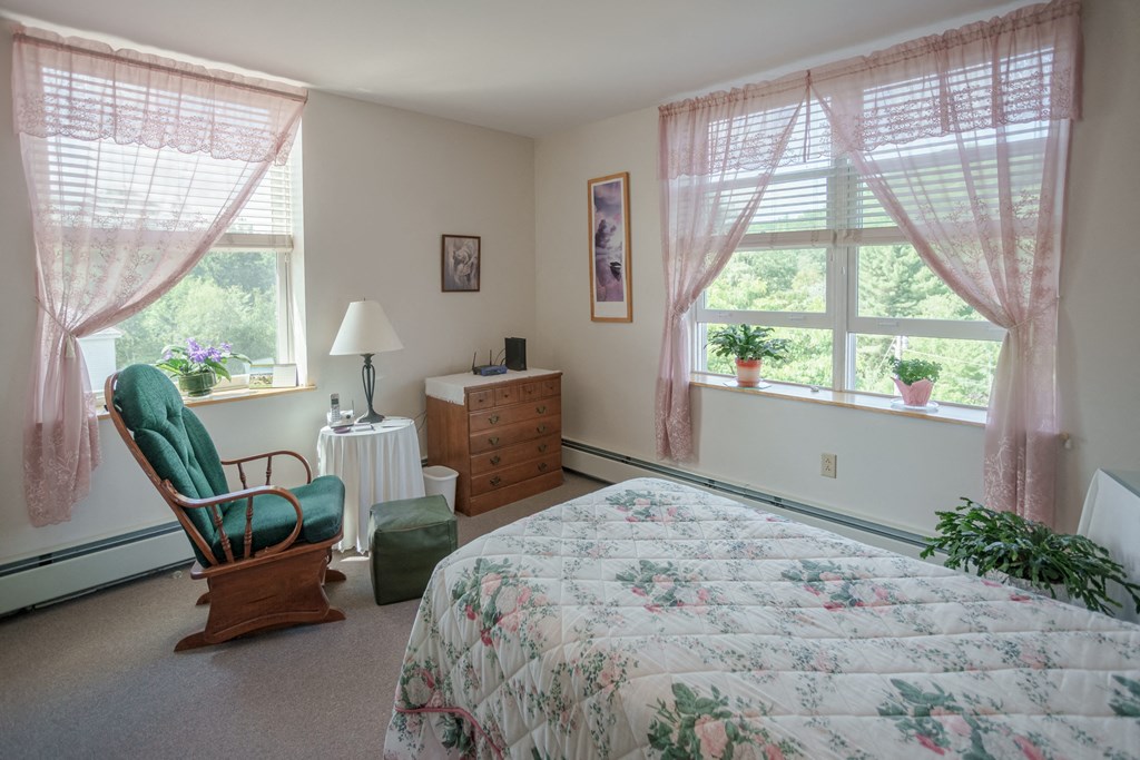 a bedroom with a bed and a chair and two windows