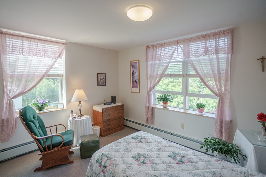 a bedroom with a bed and a chair and two windows
