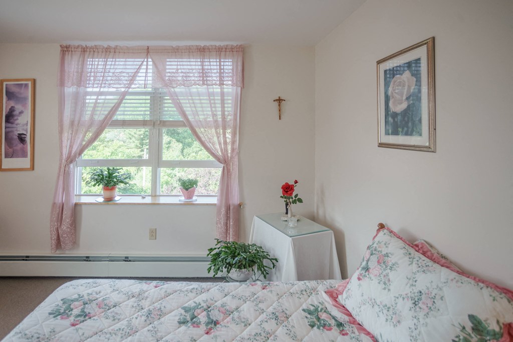 a bedroom with a bed and a window    and a table with flowers