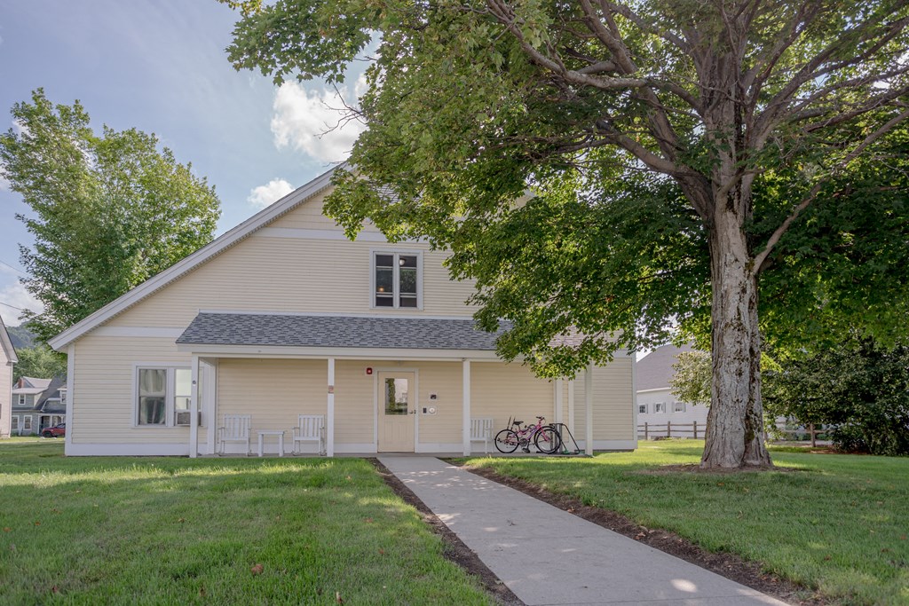 a white house with a tree and a sidewalk in front of it