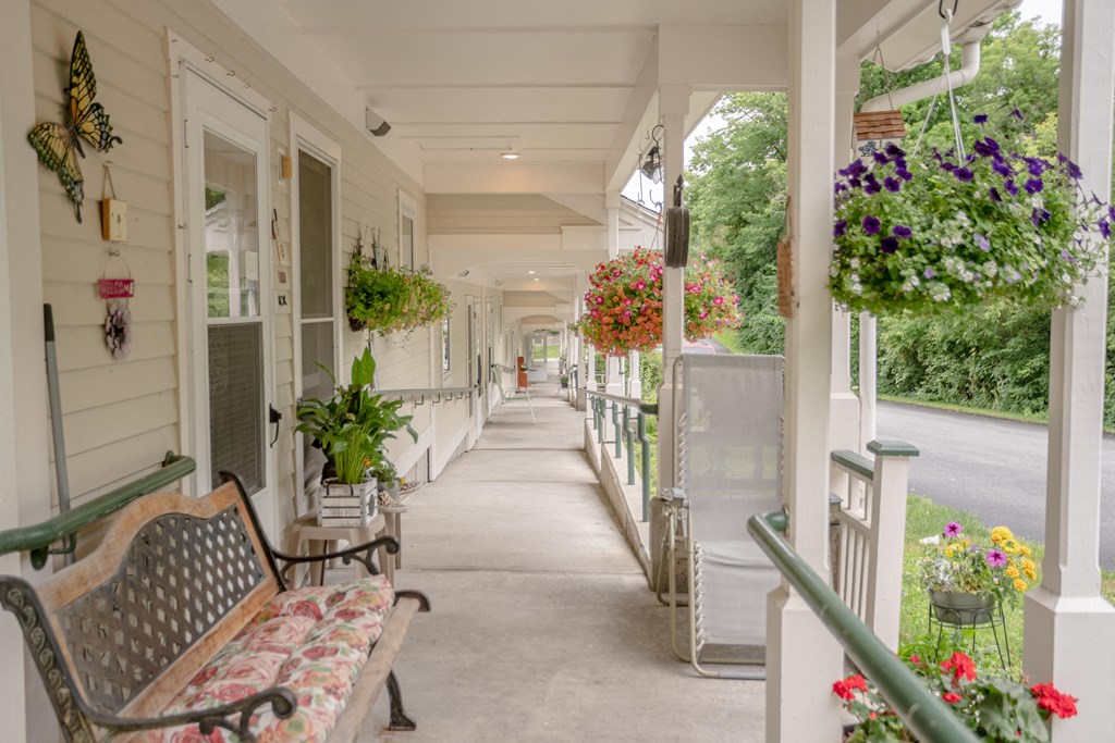 the porch of a house with benches and hanging flowers