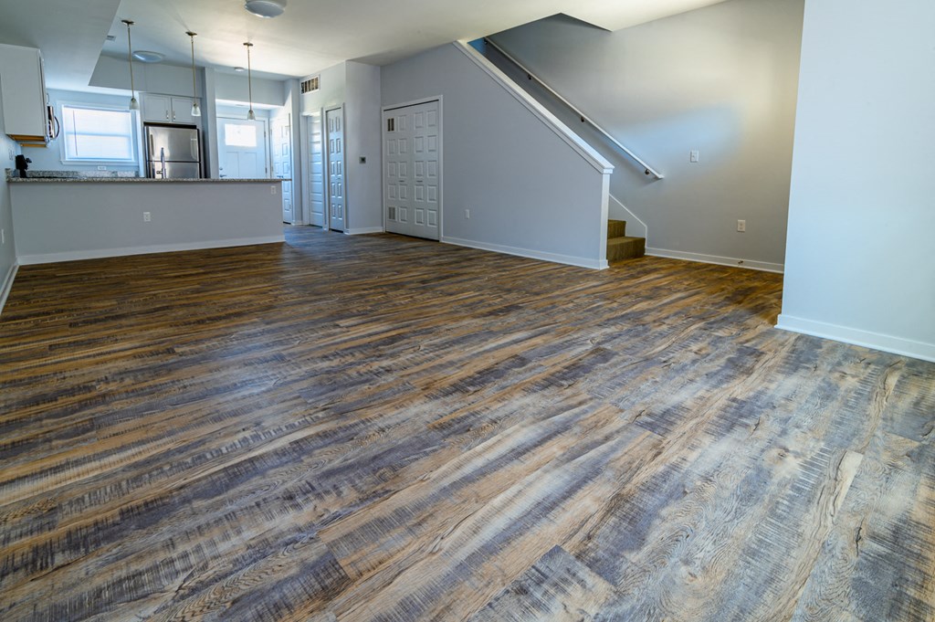 an empty living room with wood flooring and a kitchen