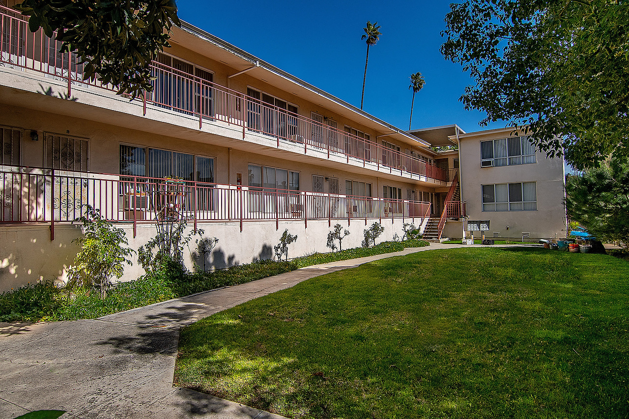 an exterior view of an apartment building with green grass and a sidewalk