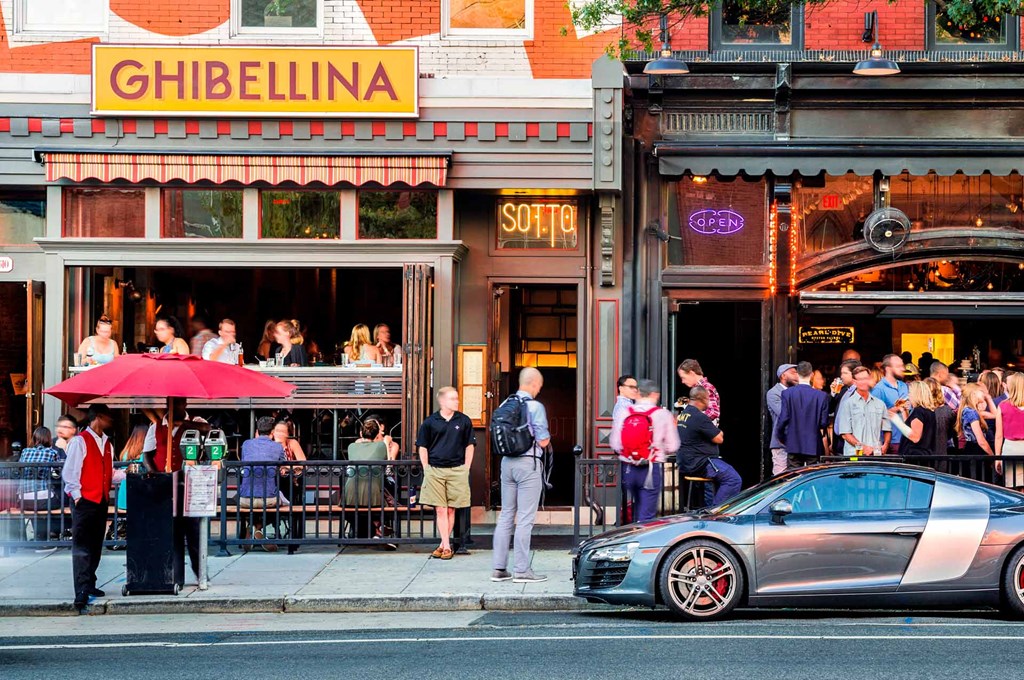 people standing outside of a bar and a car parked