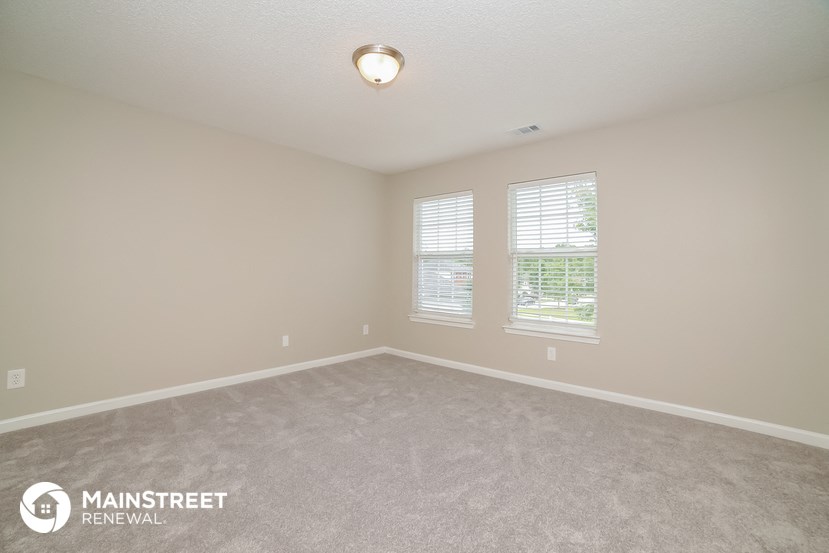 the spacious living room with two windows and carpeting