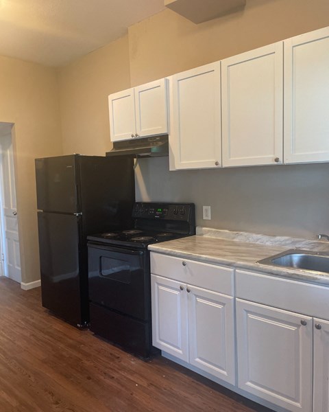 A black refrigerator and stove in a kitchen with white cabinets.