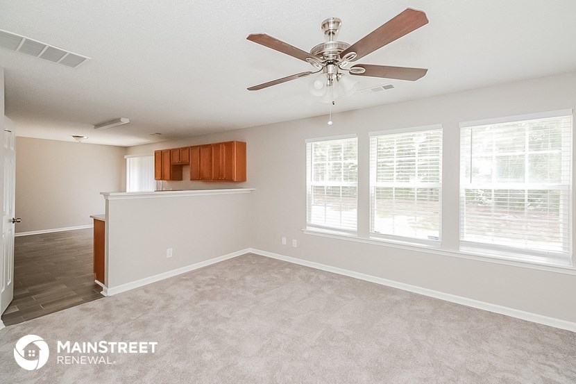 an empty living room with a ceiling fan and a kitchen