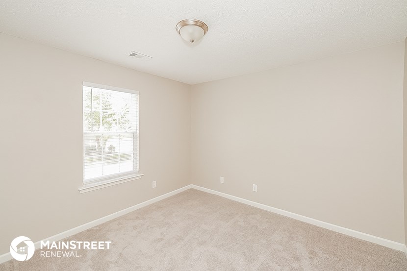 the spacious bedroom with carpeted flooring and a window