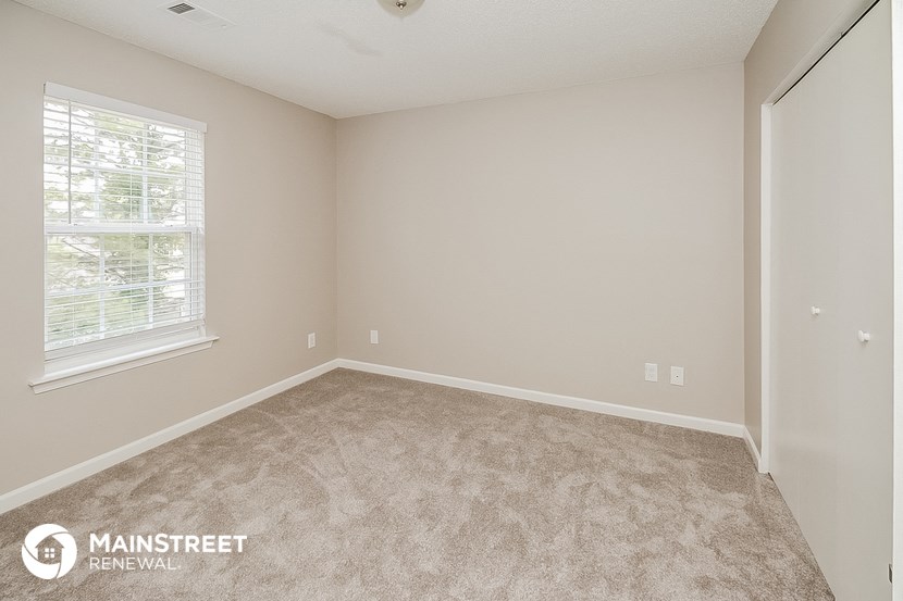 the spacious bedroom with carpeted flooring and a window