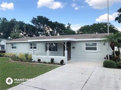 a small white house with a driveway and a tree