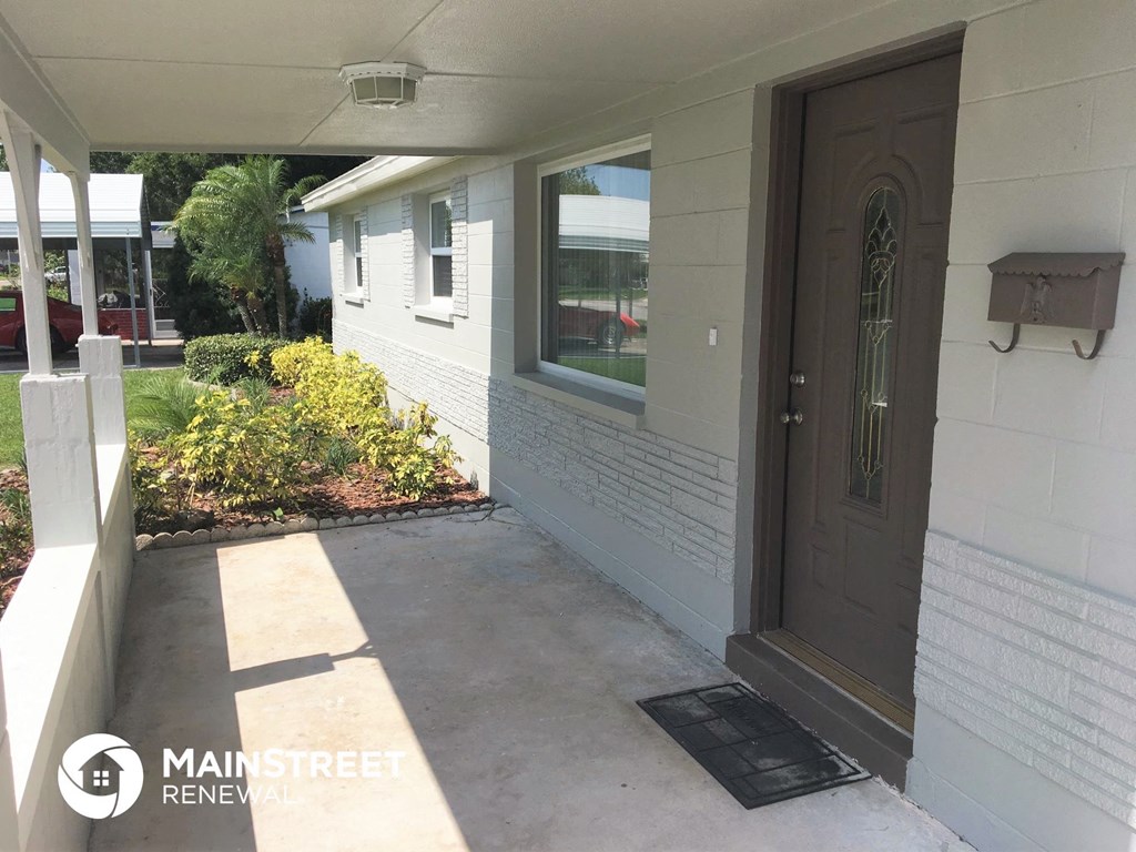 a front porch of a white house with a brown door