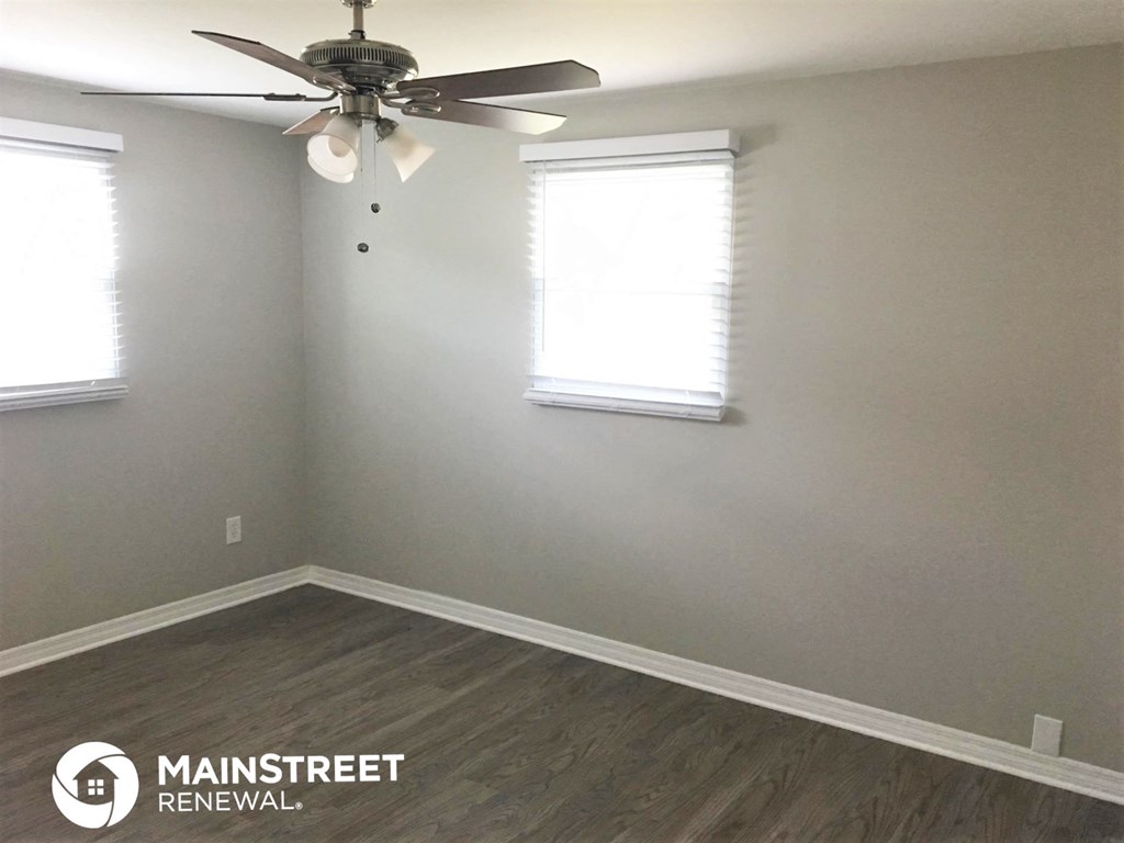 an empty room with a ceiling fan and two windows