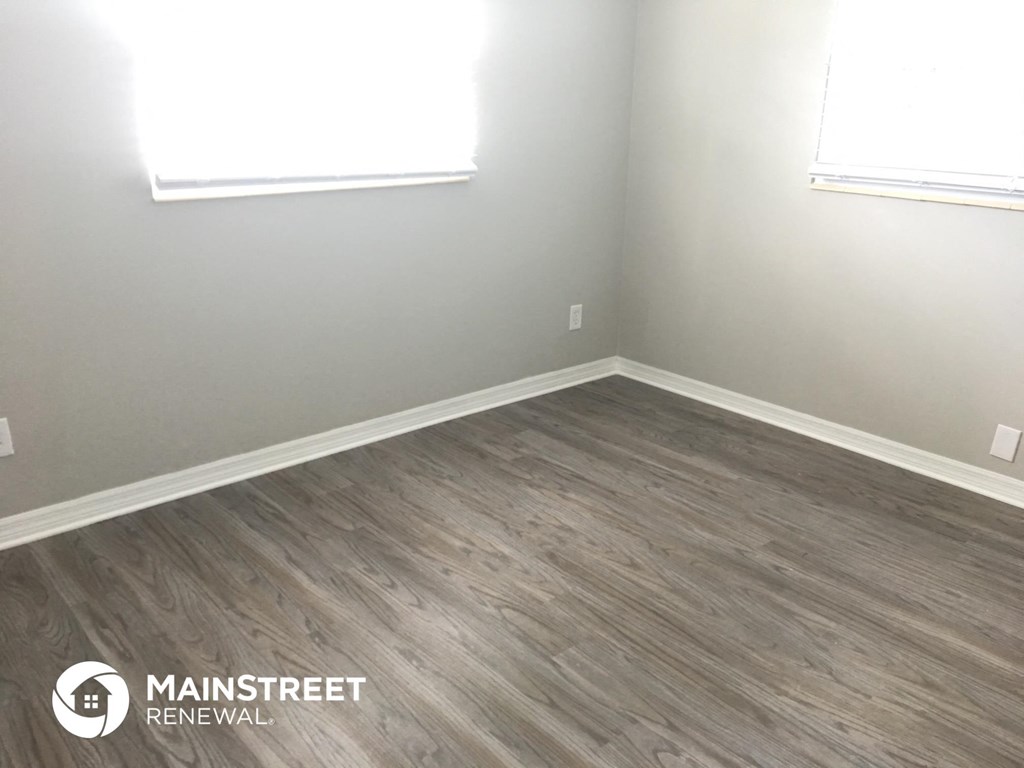 an empty room with vinyl flooring and two windows