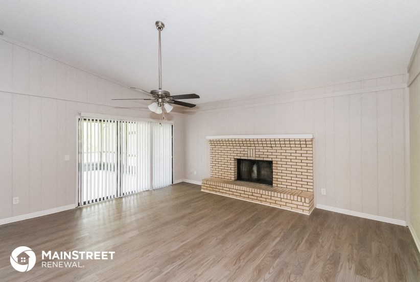 a living room with a brick fireplace and a ceiling fan