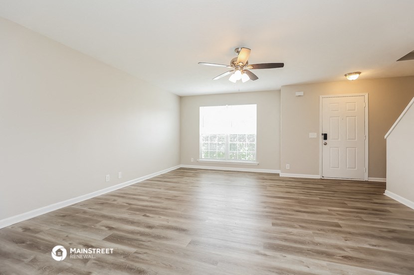 the spacious living room with a ceiling fan and a window