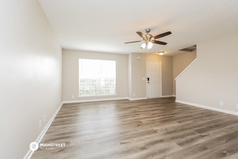 the spacious living room with hardwood floors and a ceiling fan