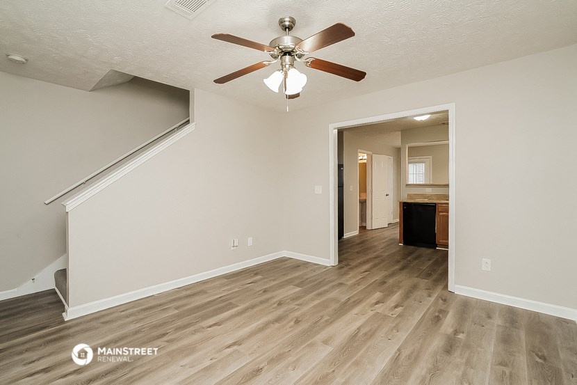 the living room and dining room of an apartment with wood floors and a ceiling fan