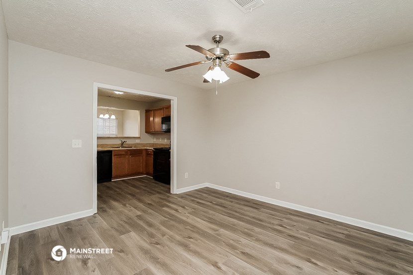an empty living room with a ceiling fan and a kitchen