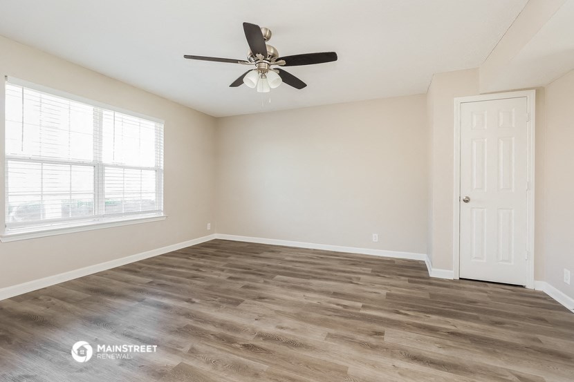the spacious living room with wood flooring and a ceiling fan