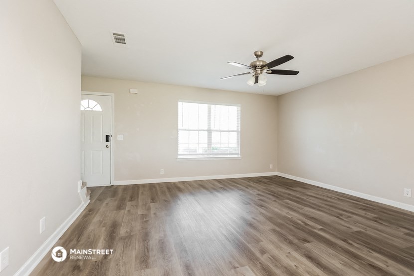 the spacious living room with wood flooring and a ceiling fan