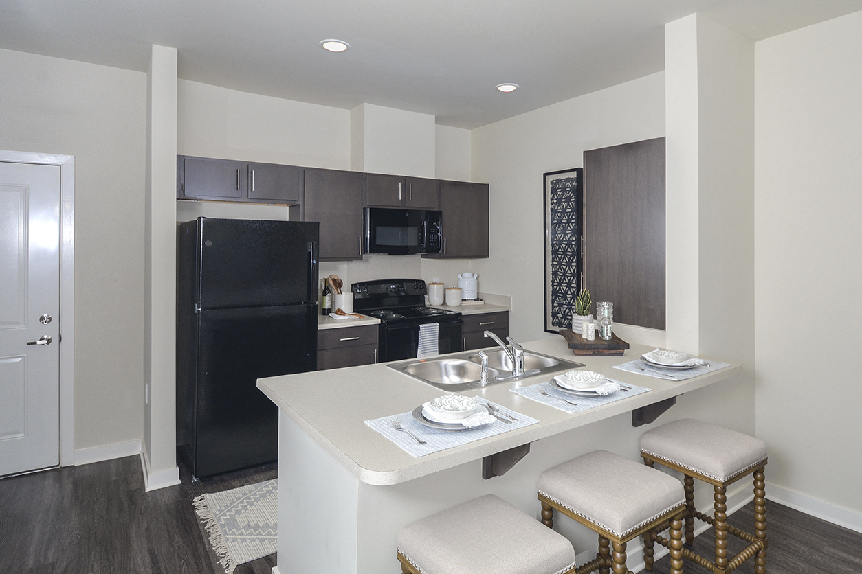 A kitchen with a black refrigerator, a white counter, and a white dining table with four chairs.