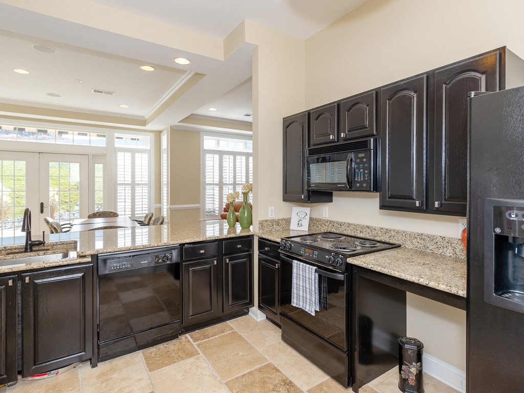 a kitchen with black cabinets and granite counter tops and a stove and a refrigerator