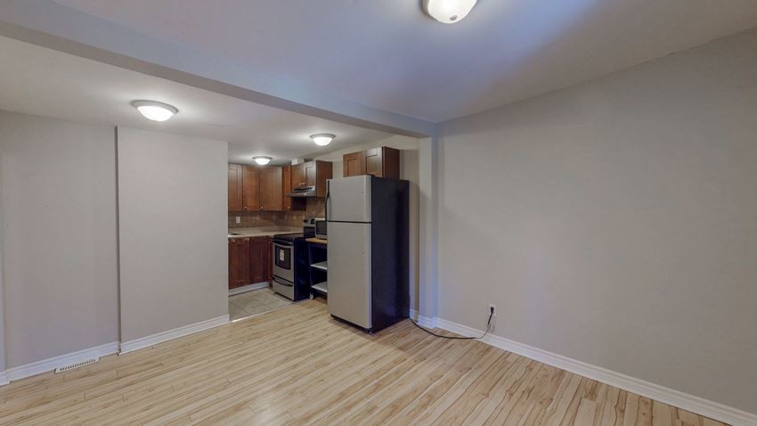 an empty living room with a refrigerator and a kitchen