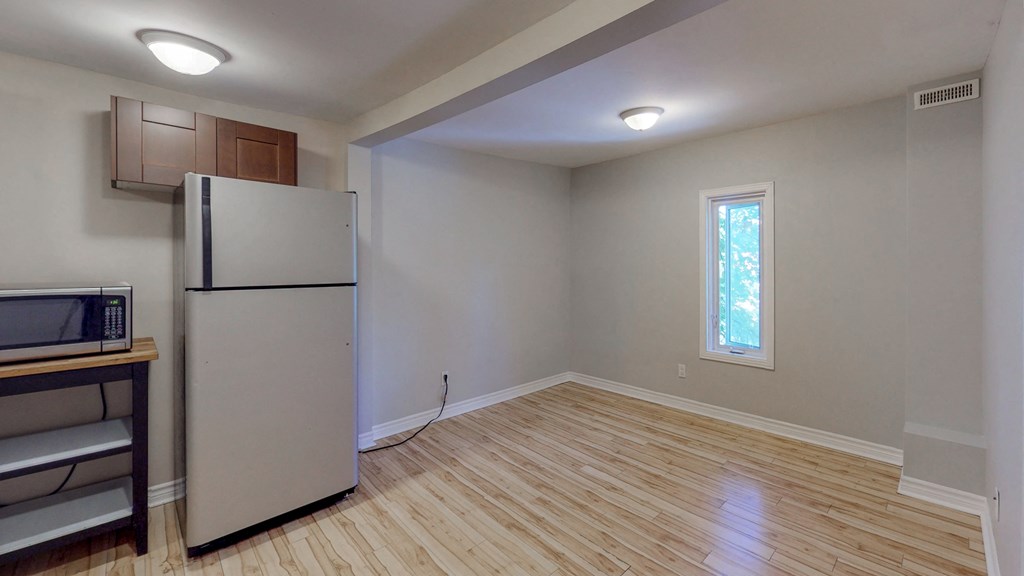 an empty living room with a refrigerator and a window
