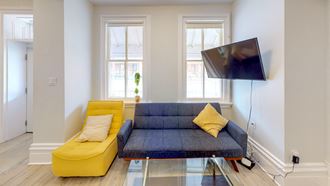 a living room with a blue couch and yellow chairs and a tv