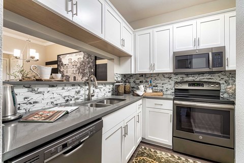 A kitchen with white cabinets and a black and white backsplash.