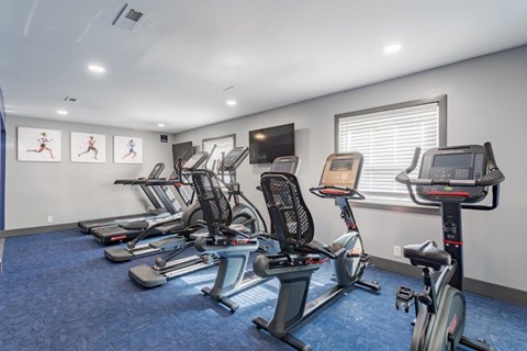 A gym with a row of stationary bikes and a television mounted on the wall.