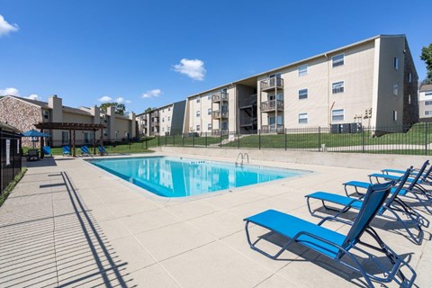 A swimming pool surrounded by blue lounge chairs and apartment buildings.