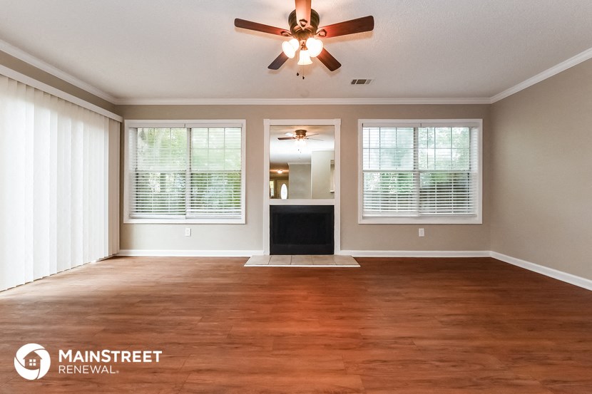 an empty living room with a ceiling fan and windows