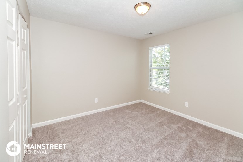 the spacious bedroom with carpeted flooring and a window