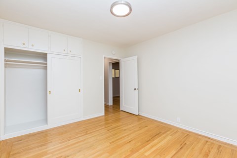 A room with white walls and wooden flooring, with a doorway leading to another room.