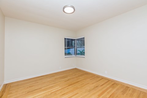 A room with wooden flooring and a window with blinds.