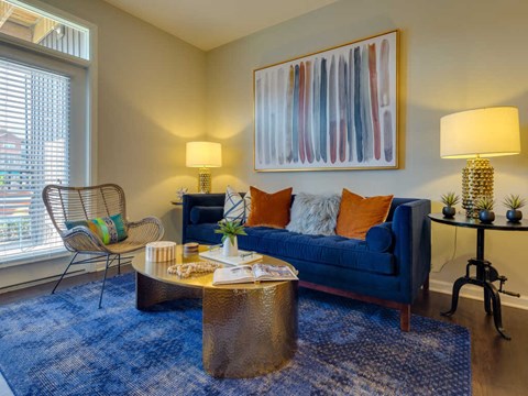 A living room with a blue couch, a chair, a coffee table, and a painting on the wall.