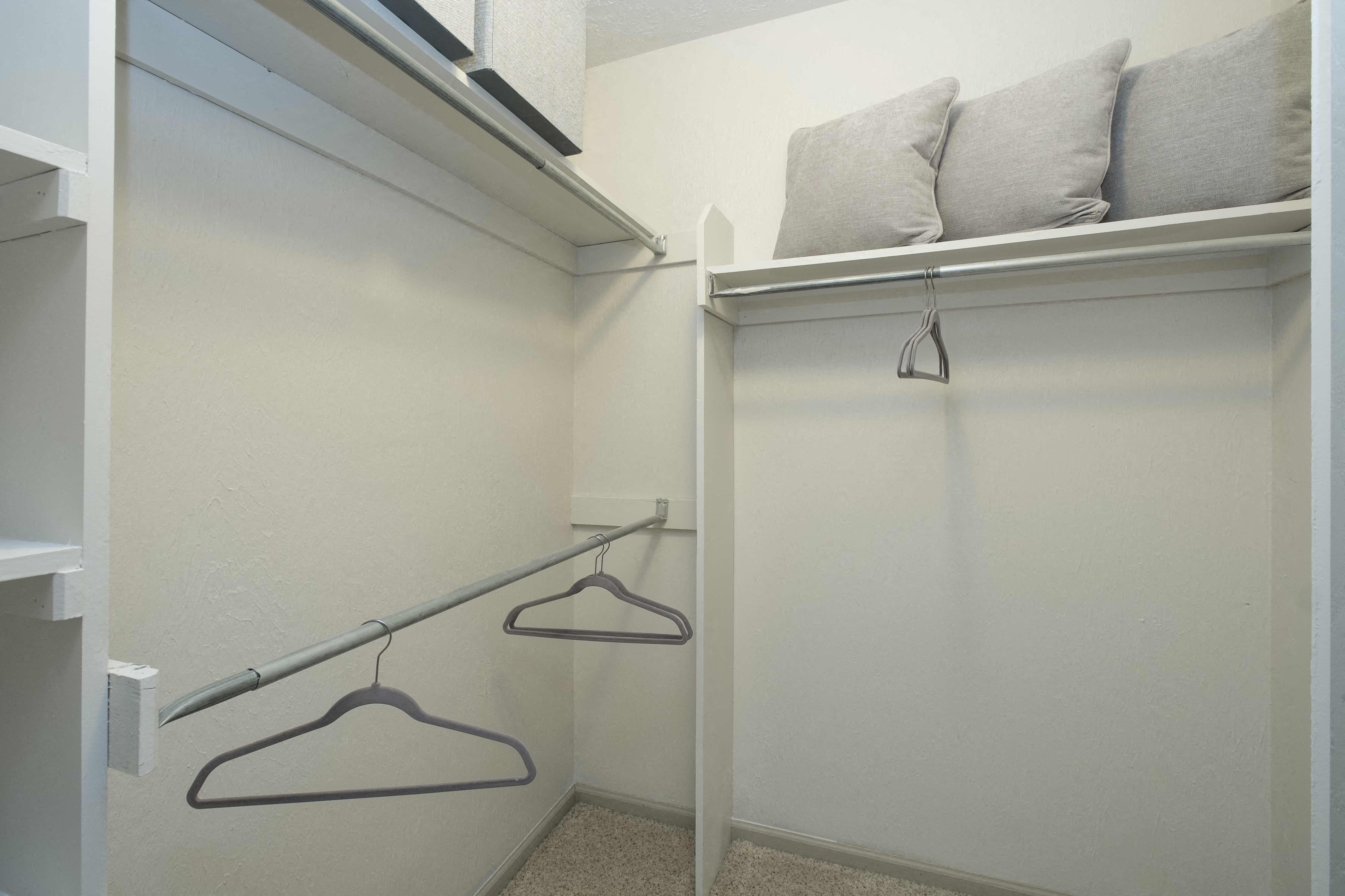 a closet with two hangers and a shelf with a pillow