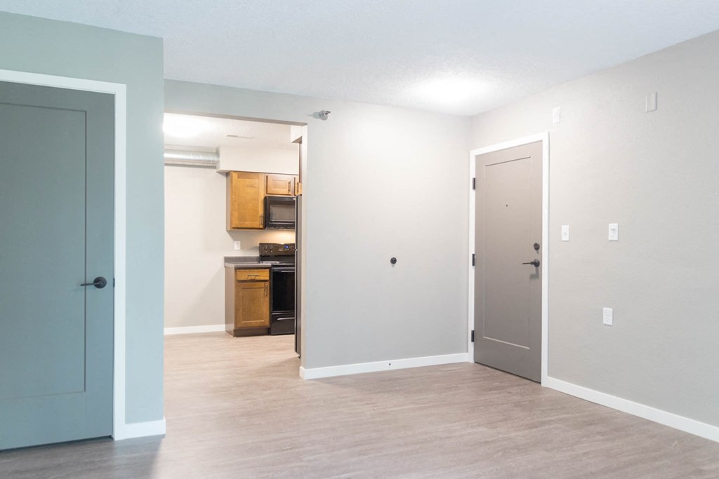 an empty living room with a door open to a kitchen