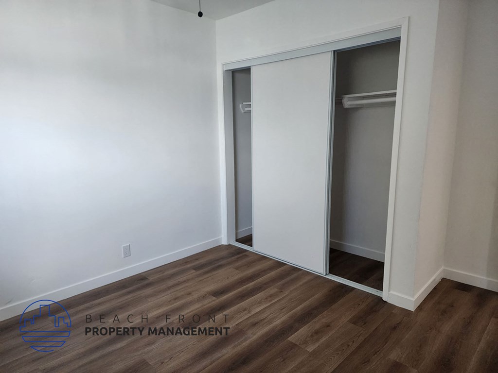 a bedroom with white walls and a closet with a wood floor