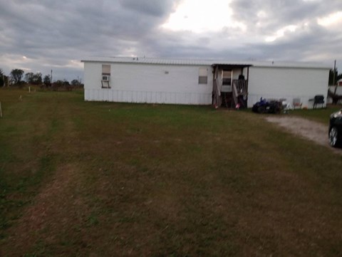 A white building with a darker roof is surrounded by a grassy field.