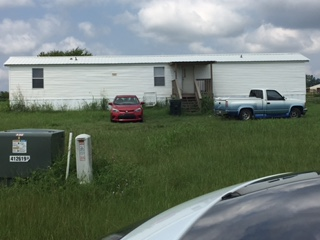 A white trailer is parked in a grassy field with a red car and a blue truck behind it.