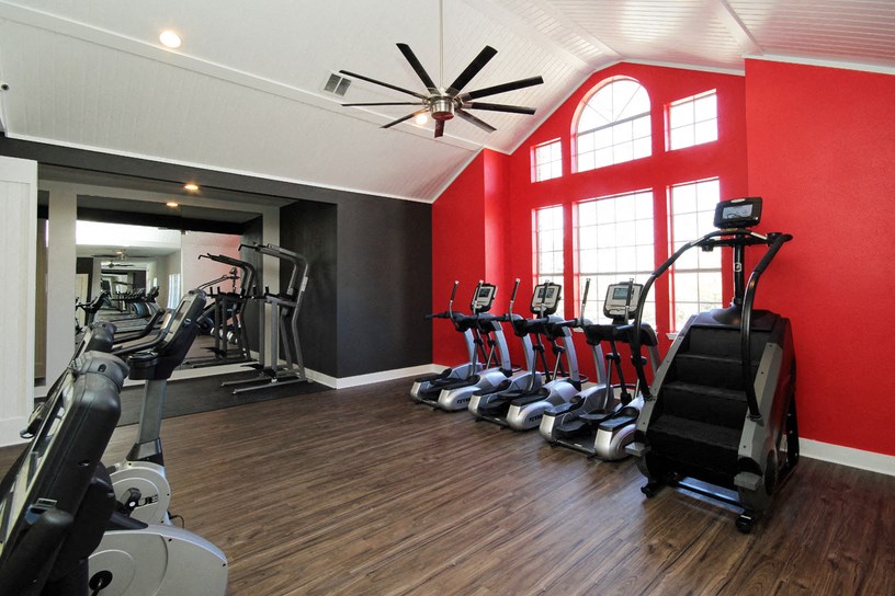 a gym with cardio machines and a ceiling fan