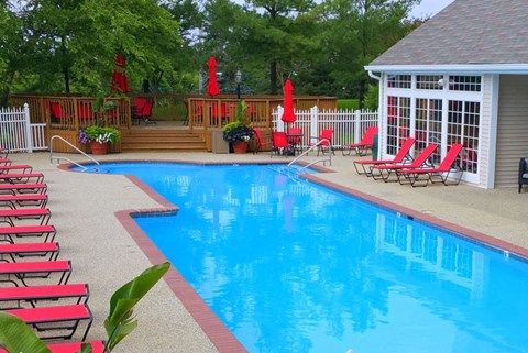 a large swimming pool with red chairs and a pool house