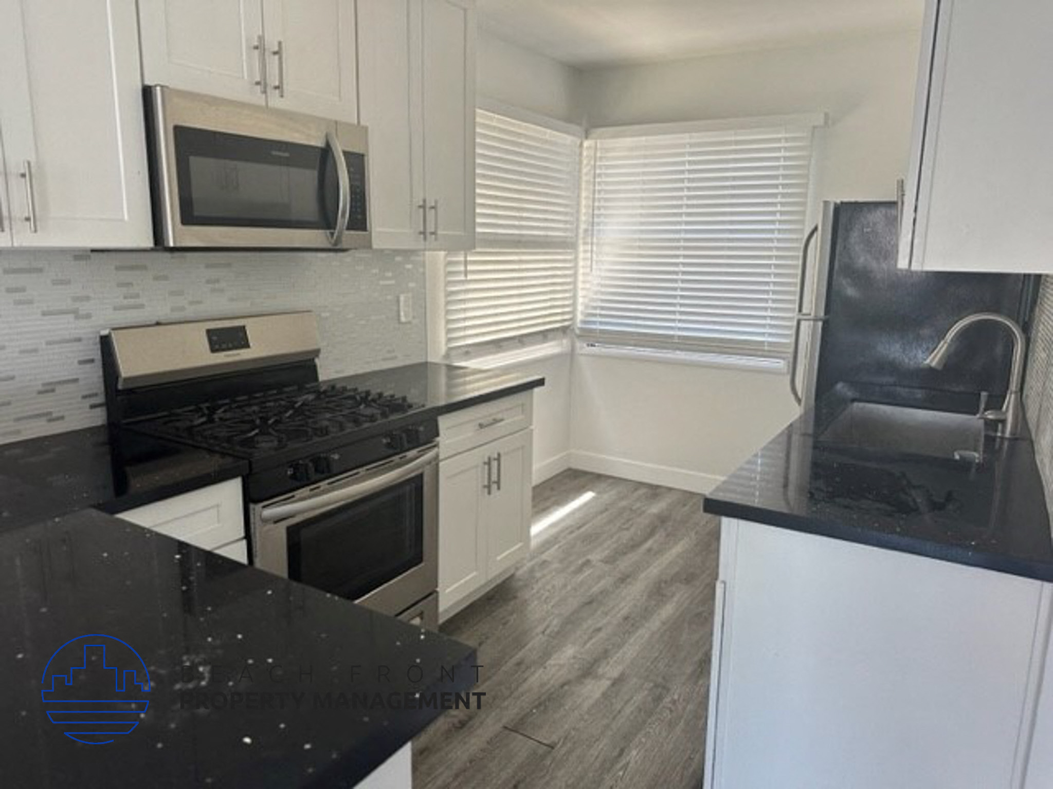 an empty kitchen with black counter tops and white cabinets