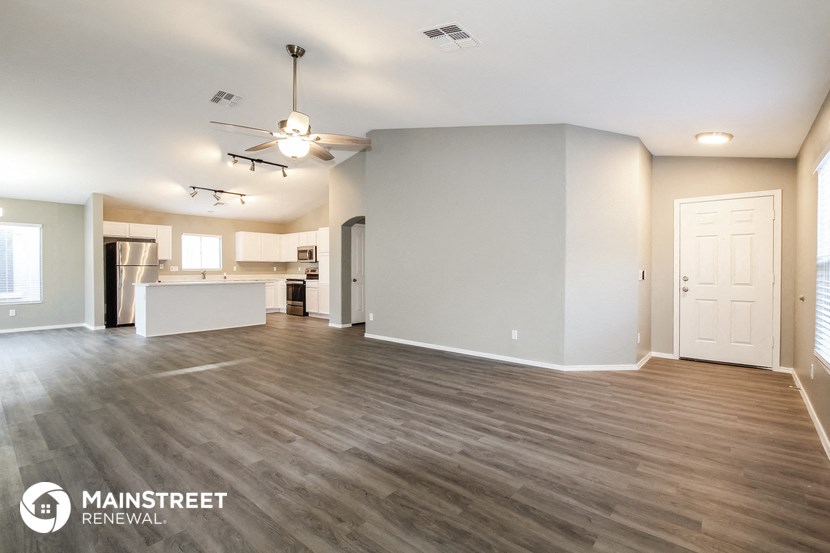 the living room and kitchen of an apartment with wood floors and a ceiling fan