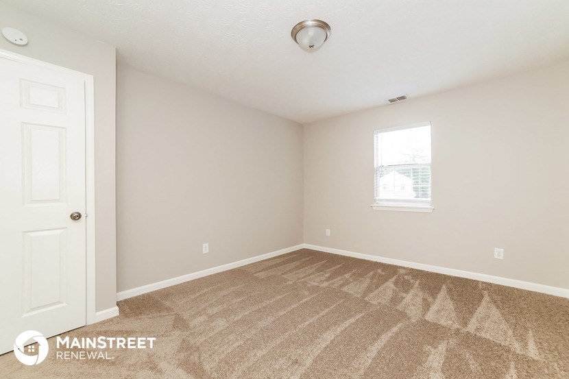 a bedroom with carpet and a white door and a window