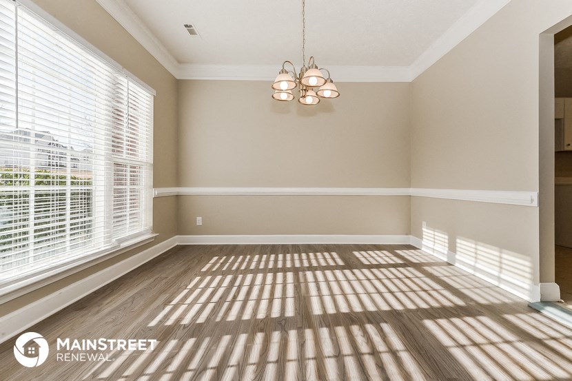 an empty living room with window blinds and a chandelier