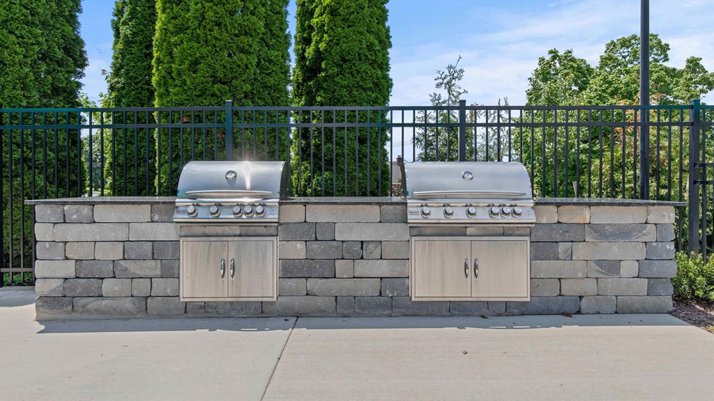 two bbq pits on a stone wall in front of a fence